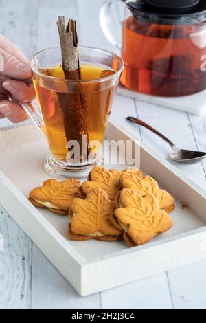 Biscuits aux épices à la citrouille sur un plateau avec une main tenant une tasse de thé aux épices à la cannelle. Banque D'Images