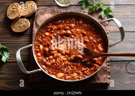 Graines de cowboy avec bœuf haché, poivre de jalapeno et bacon dans une poêle sur fond de bois.Vue rapprochée Banque D'Images