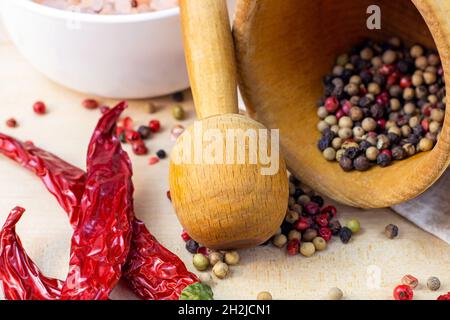 Mélanger les grains de poivre séchés dans le mortier avec le pilon, le piment sec et le sel pour cuisiner sur fond de planche à découper en bois clair dans la cuisine. Banque D'Images