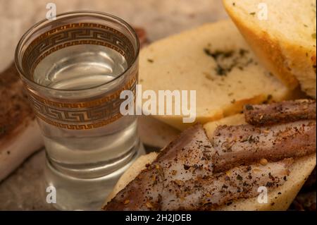 Tranches de bacon fait maison au poivre, morceaux de pain et un verre de lune maison, gros plan, mise au point sélective Banque D'Images