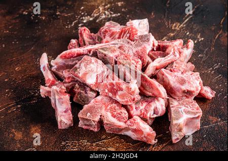Viande crue sur l'os coupée en dés pour ragoût. Arrière-plan sombre. Vue de dessus Banque D'Images