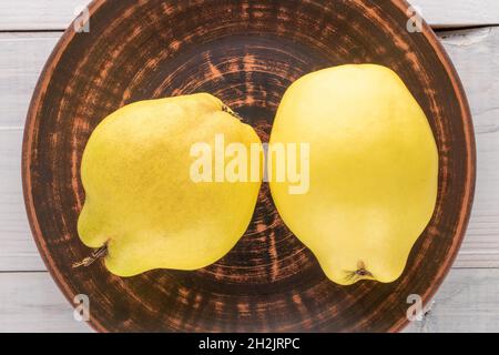 Deux coings mûrs jaune vif avec un plat de céramique sur une table en bois, vue rapprochée, vue de dessus. Banque D'Images