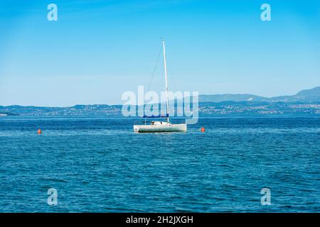 Bateau à voile blanc amarré en face de la côte du lac de Garde, près du petit village de Lazise, station touristique dans la province de Vérone, Vénétie, Italie. Banque D'Images