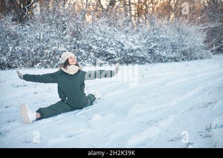 Une jeune femme en combinaison d'hiver est assise dans une ficelle longitudinale sur la neige Banque D'Images