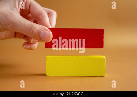 Blocs de bois vierges isolés sur fond caramel.Femme main ajoute un nouveau une pile de blocs de bois.Modèle de stratégie d'entreprise. Banque D'Images