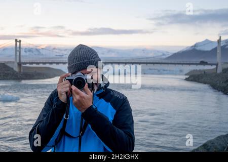 Un homme prenant une photo avec un paysage enneigé en arrière-plan en Islande Banque D'Images