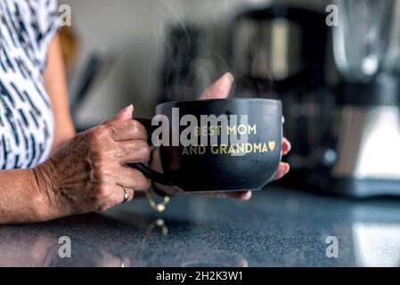 Grand-mère latin tenant une tasse noire avec un vase Banque D'Images