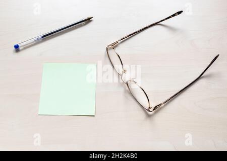 vue de dessus de lunettes, stylo bleu en plastique sur feuille de papier vierge vert sur panneau en bois brun clair Banque D'Images