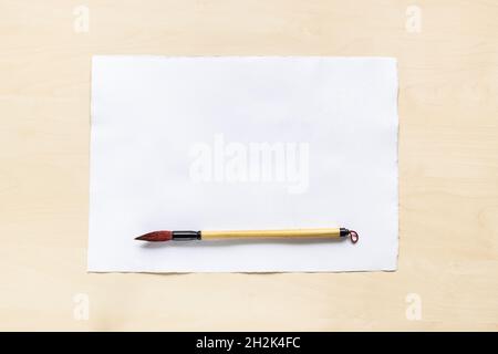 vue de dessus du pinceau de calligraphie de bambou sur une feuille vierge de papier aquarelle texturé blanc sur un panneau en bois brun clair Banque D'Images