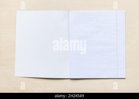 vue de dessus de la première page vierge du carnet d'école ouverte avec des feuilles carrées avec marges sur panneau en bois brun clair Banque D'Images