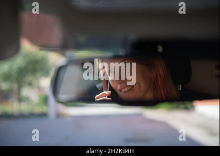 Photo d'une femme dans le rétroviseur intérieur de la voiture qui parle imprudemment sur son téléphone mobile en conduisant. Banque D'Images