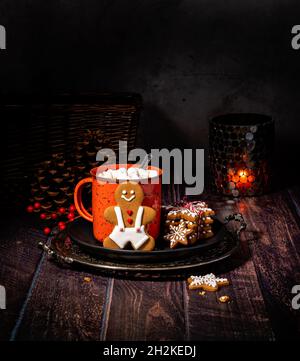 Chocolat chaud ou café fait maison dans une tasse rouge rustique avec des biscuits de Noël au pain d'épice sur une assiette comme une chaude friandise d'hiver. Banque D'Images