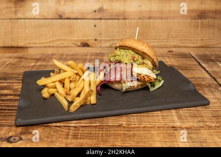 Hamburger mexicain au poulet avec guacamole, fromage à la crème, bacon fumé, laitue et Emmental fondu avec frites Banque D'Images