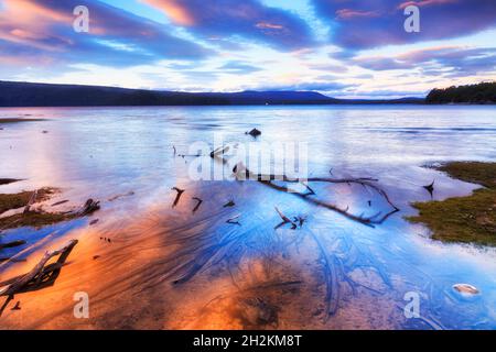 Reflets colorés des nuages de ciel illuminés par le soleil dans le lac St clair de Tasmanie au lever du soleil. Banque D'Images