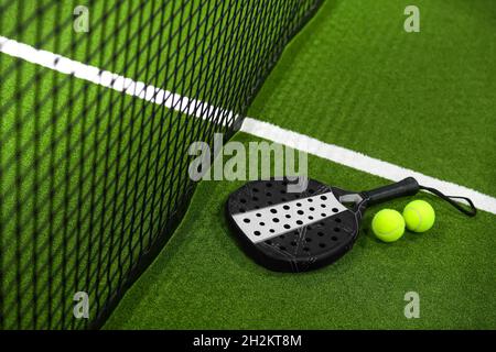 Vue rapprochée d'une raquette à paddle et de balles dans un terrain de padel de tennis près du filet.Arrière-plan vert avec lignes blanches.Sport, santé, jeunesse et loisirs Banque D'Images