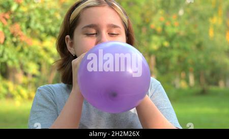 une adolescente gonfle un ballon lilas de près sur le fond de la nature. Banque D'Images