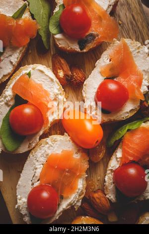 séchez le saumon fumé vieilli sur les tranches de pain et les sandwichs au fromage à la crème avec des tomates cerises et de la salade de roquette. vue rapprochée Banque D'Images