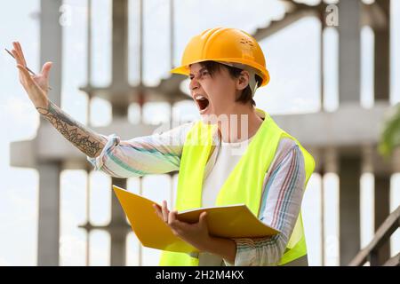 Femme en colère ouvrier de construction dans hardhat avec dossier à l'extérieur Banque D'Images
