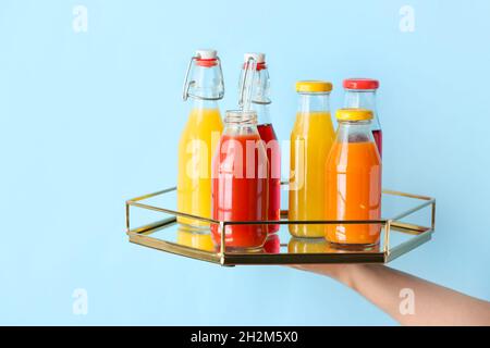 Main femelle avec des bouteilles de jus sain sur fond de couleur Banque D'Images