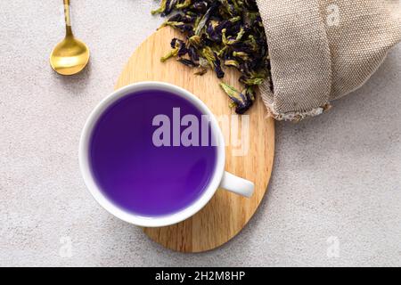 Tasse avec thé bleu et sac avec fleurs de pois de papillon séchées sur fond clair Banque D'Images
