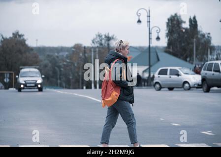 une fille avec un sac à dos traverse la route sur la chaussée à un passage piéton devant les voitures qui passent. Banque D'Images