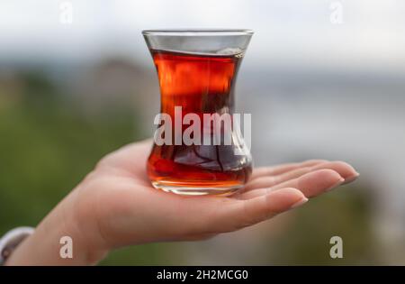 Tasse de thé Armudas sur la paume de la main de femme, thé turc traditionnel sur fond de l'Istanbul, Sile paysage urbain. Verre d'Armuda avec thé. Dos flou Banque D'Images