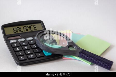 Calculatrice avec le texte Balance sur fond blanc, près d'une loupe et des autocollants de couleur.Affaires, finance, banque conceptuelle. Banque D'Images