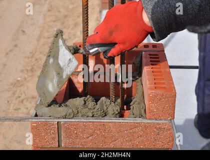 Ouvrier de bricklayer installation de blocs rouges et calfeutrage de briques joints de maçonnerie mur extérieur avec couteau à pâte à truelle extérieur Banque D'Images