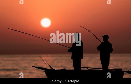 Vieux amis pêche au coucher du soleil sur la mer. Deux pêcheurs Silhouette pêche ensemble sur un petit bateau. Vie simple et heureuse Banque D'Images