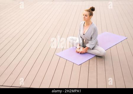 Gros plan d'une jeune femme calme assise sur un tapis de yoga avec les yeux fermés et méditant dans la posture du papillon, en inclinant la tête vers l'avant. Banque D'Images