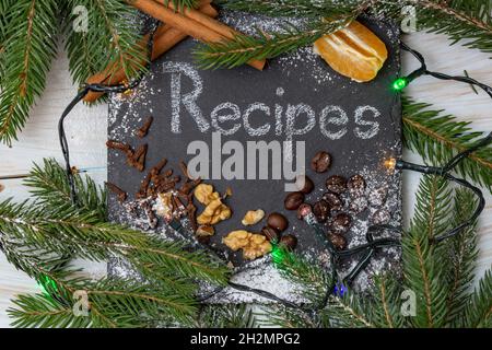 Recettes de Noël ou d'hiver, mot écrit sur une tuile de pierre noire avec de la craie blanche, entourée de branches de sapin, de grains de café, de cannelle, d'épices, waln Banque D'Images