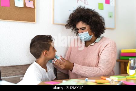 Femme enseignante donnant un masque de protection du visage à l'élève en classe préscolaire pendant une pandémie de virus corona - concept de soins de santé et d'éducation Banque D'Images