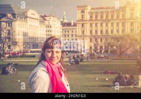 Jeune fille voyageur avec veste blanche regardant loin et sourire dans le parc Sigmund Freud du centre historique de Vienne avec vieux bâtiments arrière-plan, wom Banque D'Images