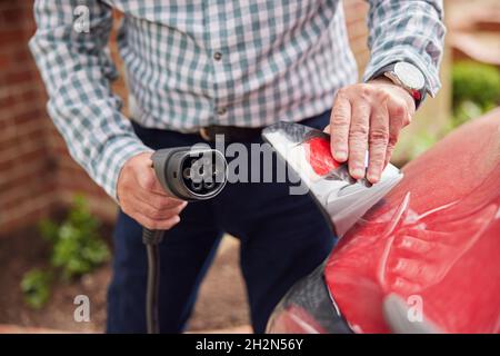 Gros plan de l'homme qui attache le câble de chargement à la voiture électrique écologique sans émission à la maison Banque D'Images
