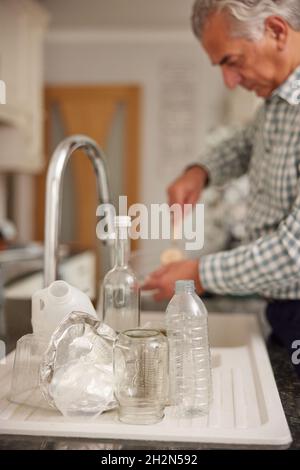 Homme mature à la maison dans la cuisine laver emballages usagés avant recyclage Banque D'Images