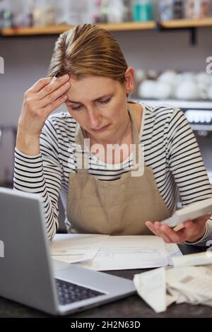 Femme inquiète propriétaire du café en difficulté financière Via des factures utilisant un ordinateur portable et une calculatrice Banque D'Images