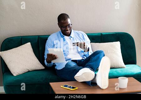 Homme souriant payant par carte de crédit tout en utilisant une tablette numérique à la maison Banque D'Images
