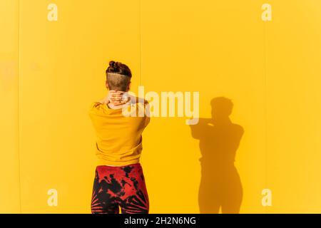 Femme avec les mains sur le cou debout devant le mur jaune Banque D'Images