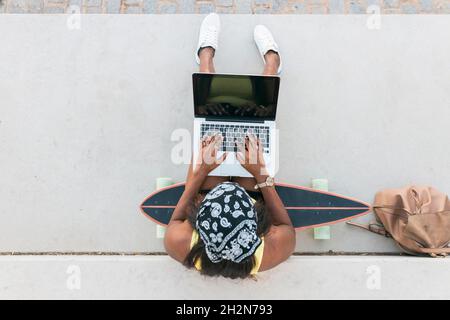 Femme portant un foulard à l'aide d'un ordinateur portable assis sur un skateboard Banque D'Images