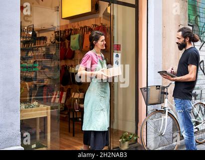 Entrepreneur féminin tenant le paquet tout en parlant avec le liveur mâle à l'extérieur du magasin Banque D'Images