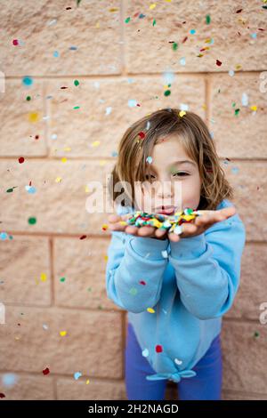 Fille aux cheveux bruns soufflé confetti colorés devant le mur Banque D'Images