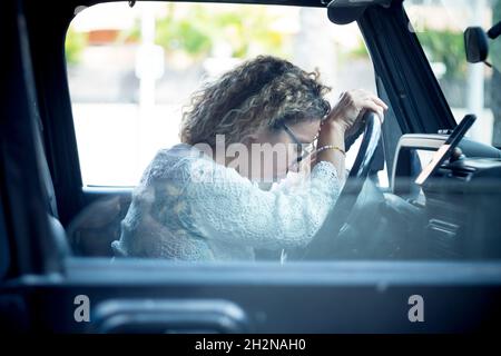 Femme mûre fatiguée avec des cheveux bouclés assis en voiture Banque D'Images