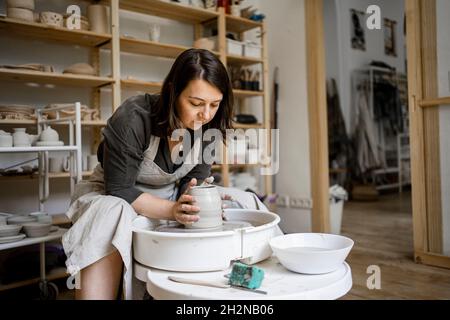 Jeune femme potter moulant l'argile tout en travaillant dans l'atelier Banque D'Images