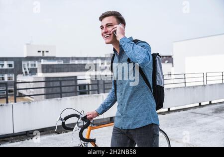 Un jeune homme heureux avec un vélo parlant sur un smartphone Banque D'Images