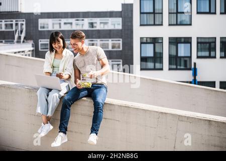 Des amis hommes et femmes heureux partageant un ordinateur portable pendant la journée ensoleillée Banque D'Images