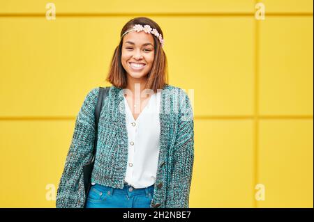 Femme souriante portant le tiara de fleur debout devant le mur jaune Banque D'Images