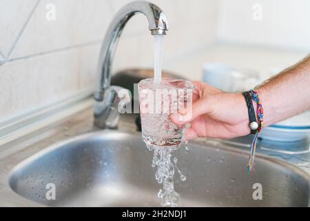 Homme remplissant le verre avec de l'eau à l'évier dans la cuisine Banque D'Images