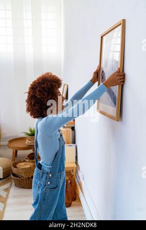 Femme REDHEAD installant le cadre photo sur un mur blanc Banque D'Images