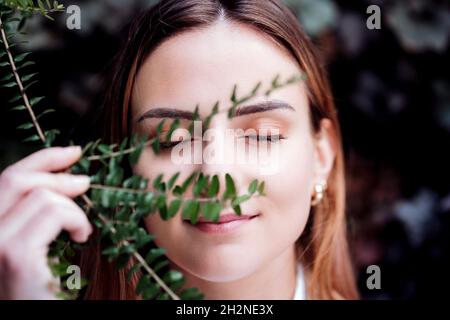 Femme d'affaires souriante avec les yeux fermés tenant l'usine devant le visage Banque D'Images