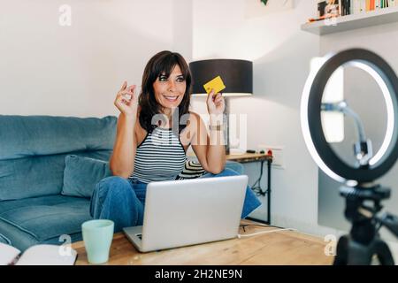 Enregistreur de données femme souriante avec carte de crédit filmant via un smartphone dans le salon Banque D'Images